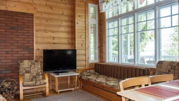 Ein gemütliches Blockhäuschen-Interieur mit Fernseher, Sitzecke und großen Fenstern.