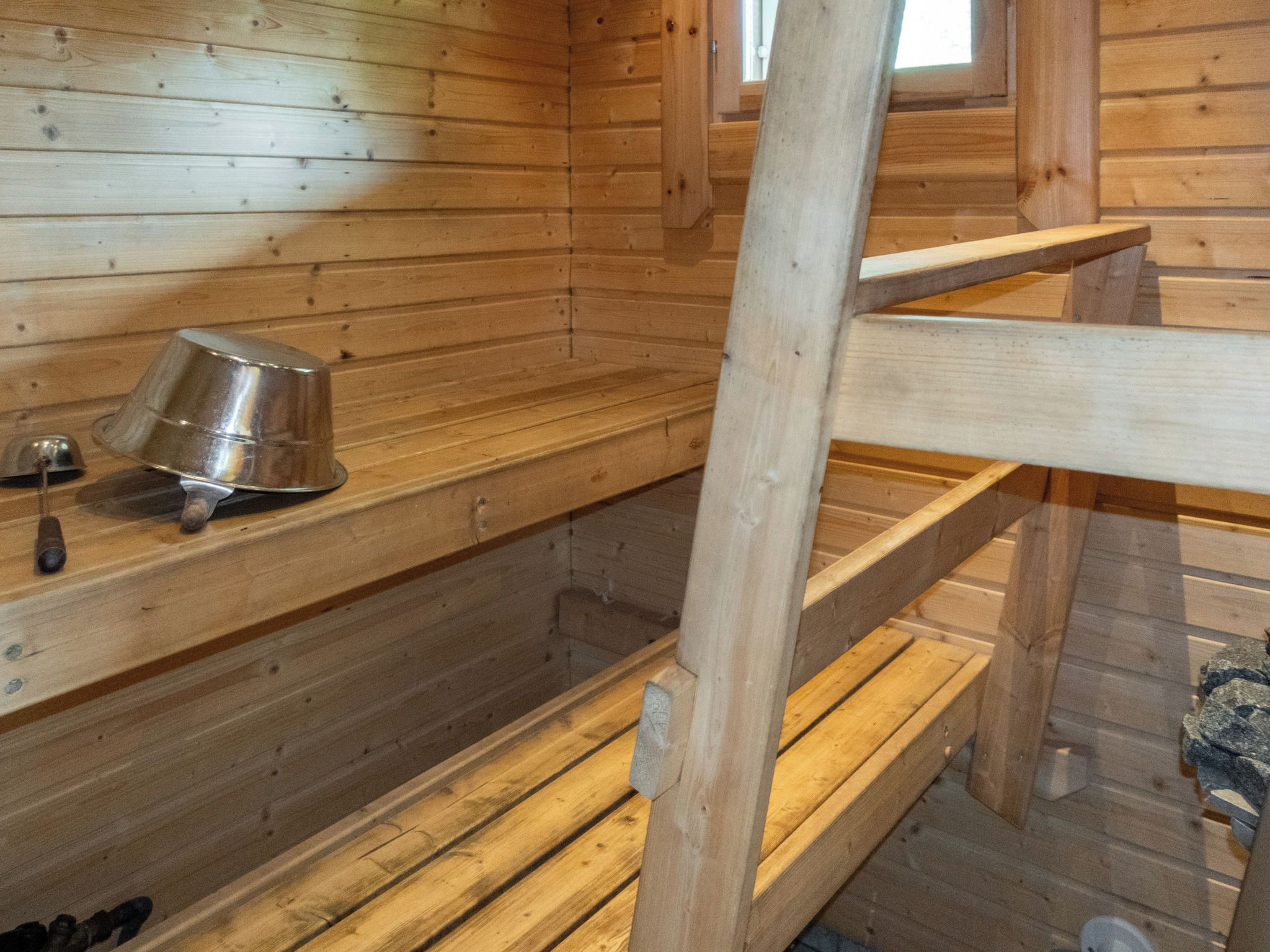 Una sauna de madera con bancos y un recipiente metálico.