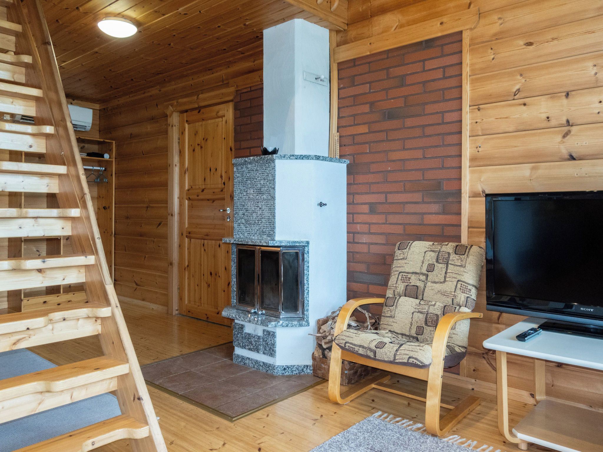 A wooden interior with a fireplace, a TV, and a chair.