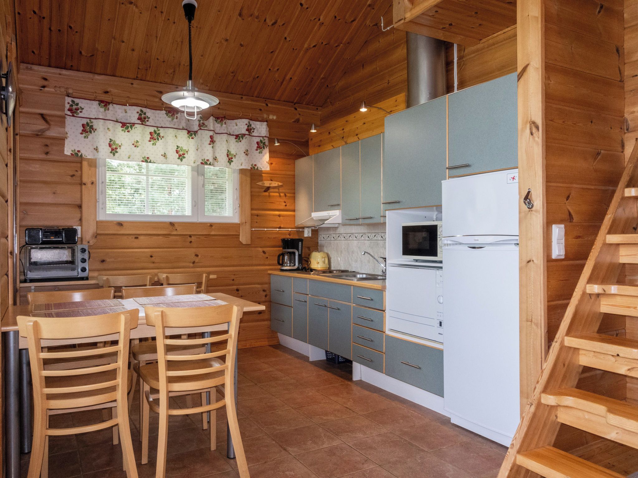 A wooden cabin interior with a kitchen, dining area, and a staircase.