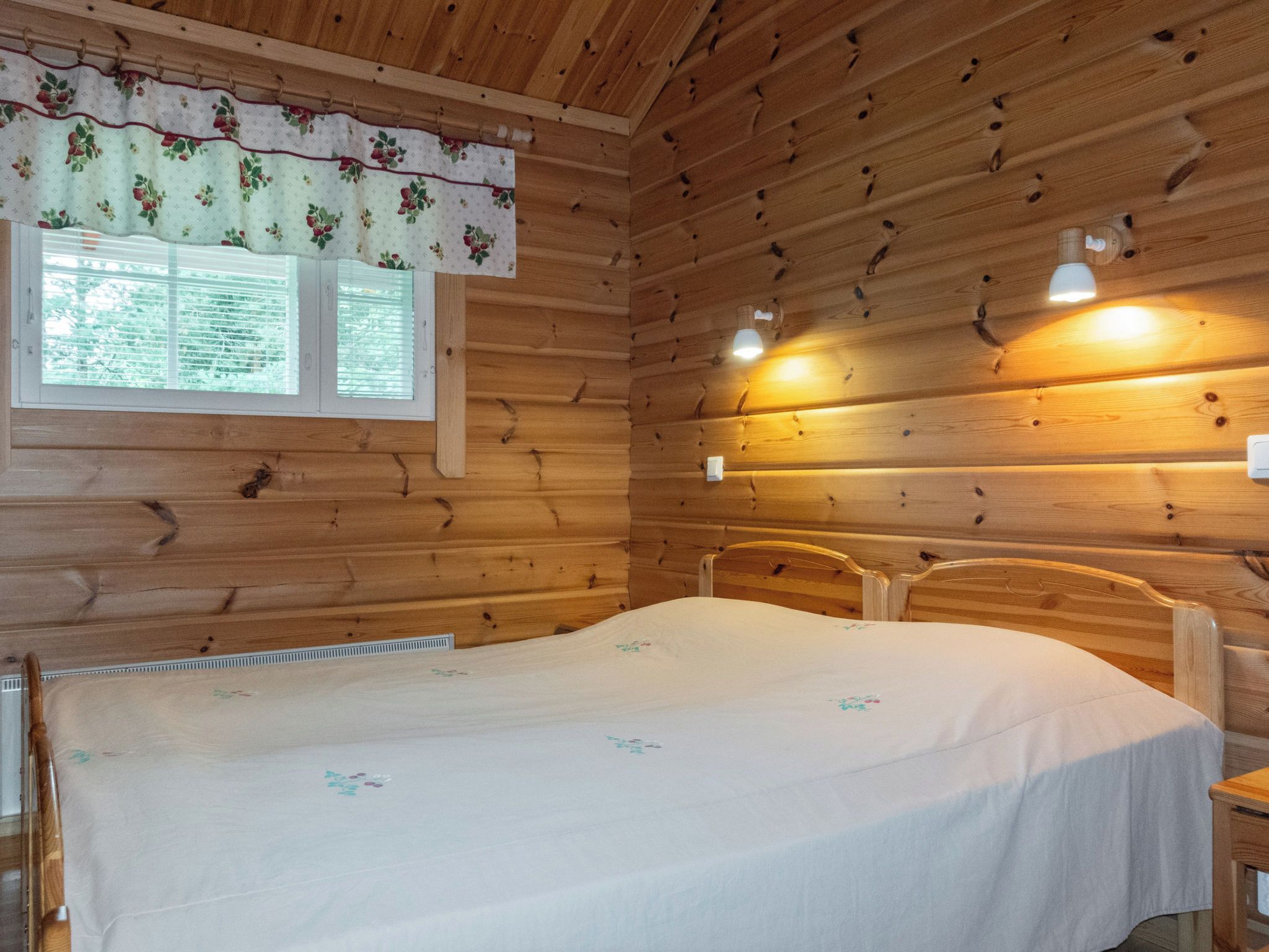 Une chambre de style cabane en bois, avec un lit, une fenêtre équipée de stores et deux lampes fixées au mur.
