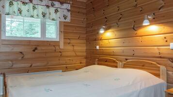 Une chambre de style cabane en bois, avec un lit, une fenêtre équipée de stores et deux lampes fixées au mur.