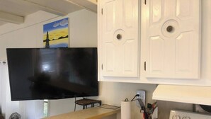 Eine Küche mit weißen Schränken, einem Flachbildfernseher, einer Holz Arbeitsplatte, einem Herd und einem Bild an der Wand.