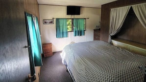 Ein Schlafzimmer mit Bett, Fernseher, Schminktisch und einem Fenster mit Vorhängen.