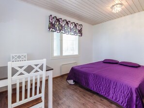 A bedroom with a bed, a chair, a window with blinds, and a ceiling light fixture.