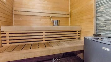 A sauna with a wooden bench, a metal bucket, and a stone wall.