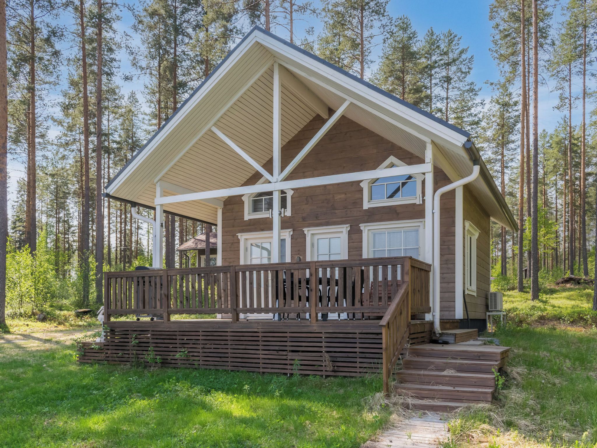 A cabin with a wooden deck, a covered porch, and a view of a forest.