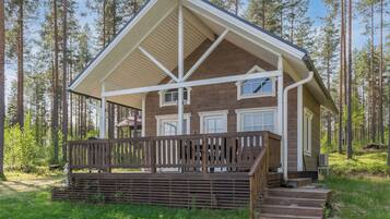 A cabin with a wooden deck, a covered porch, and a view of a forest.