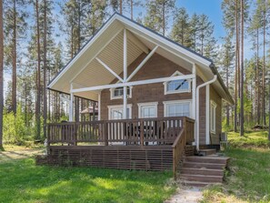 A cabin with a wooden deck, a covered porch, and a view of a forest.