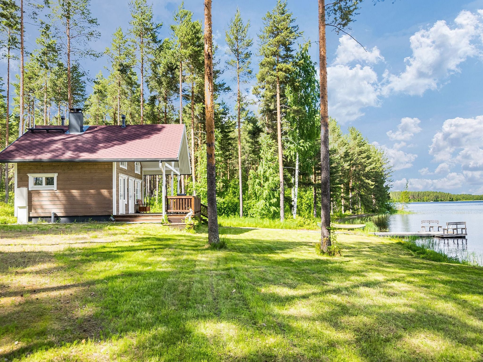 A cabin with a deck, surrounded by tall trees and a lake.