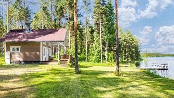 A cabin with a deck, surrounded by tall trees and a lake.