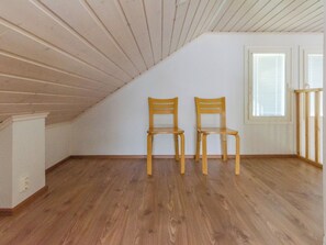 Habitación en ático con suelo de madera, dos sillas de madera, una ventana con persianas y una pared blanca.
