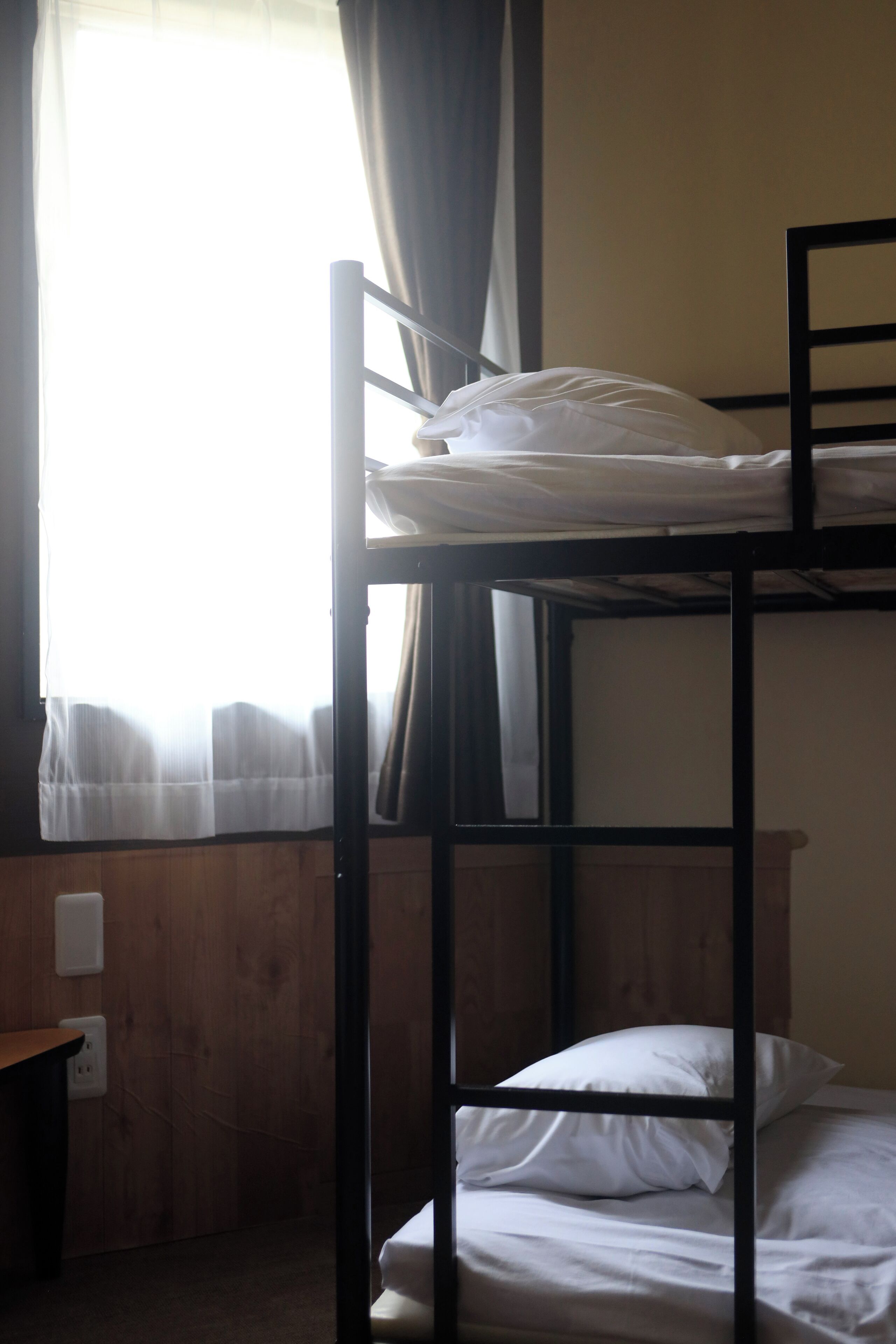 Ein Etagenbett mit weißer Bettwäsche, ein Holztisch und ein Fenster mit Vorhängen.