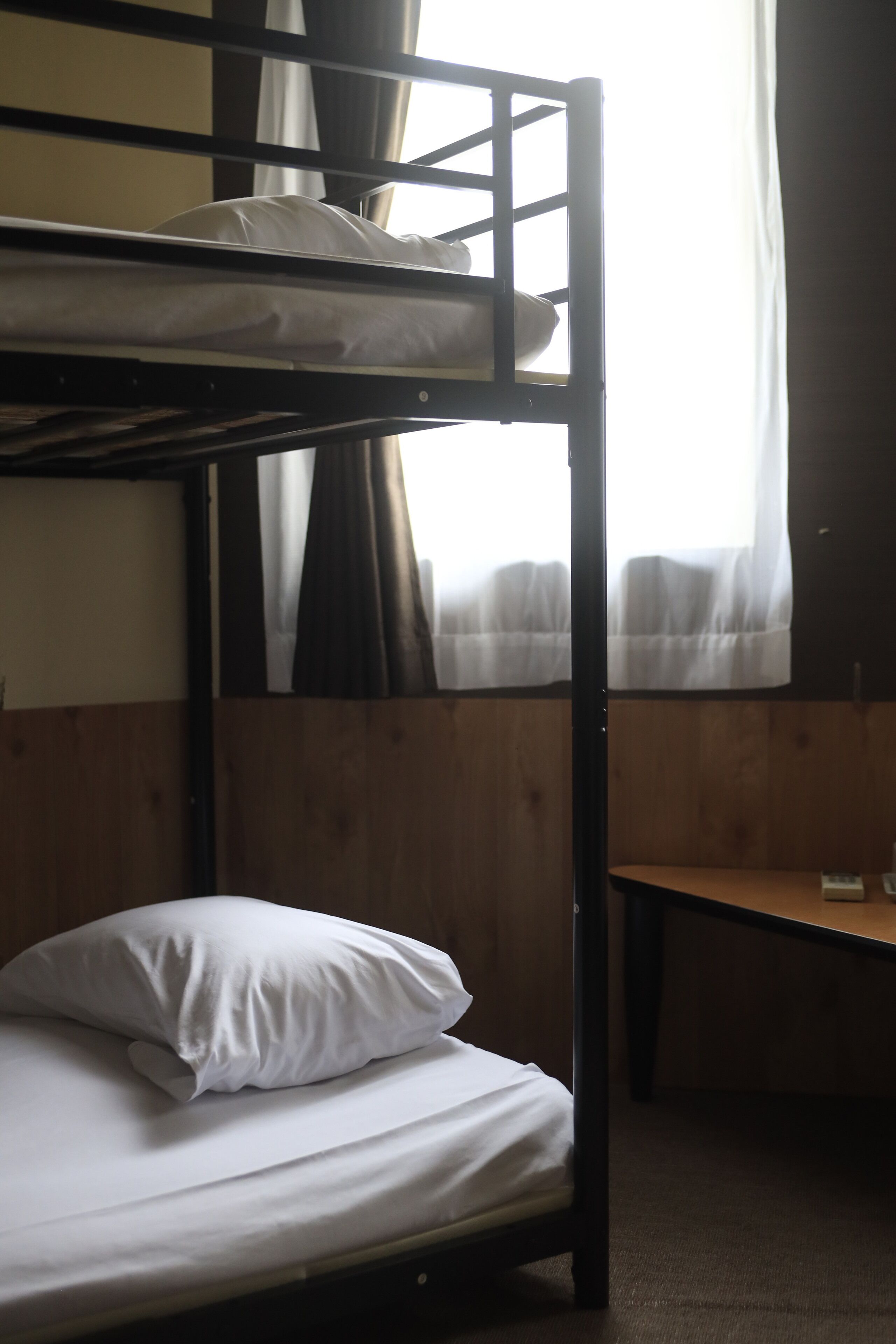 A bunk bed with a pillow, a wooden desk, and a window with curtains.