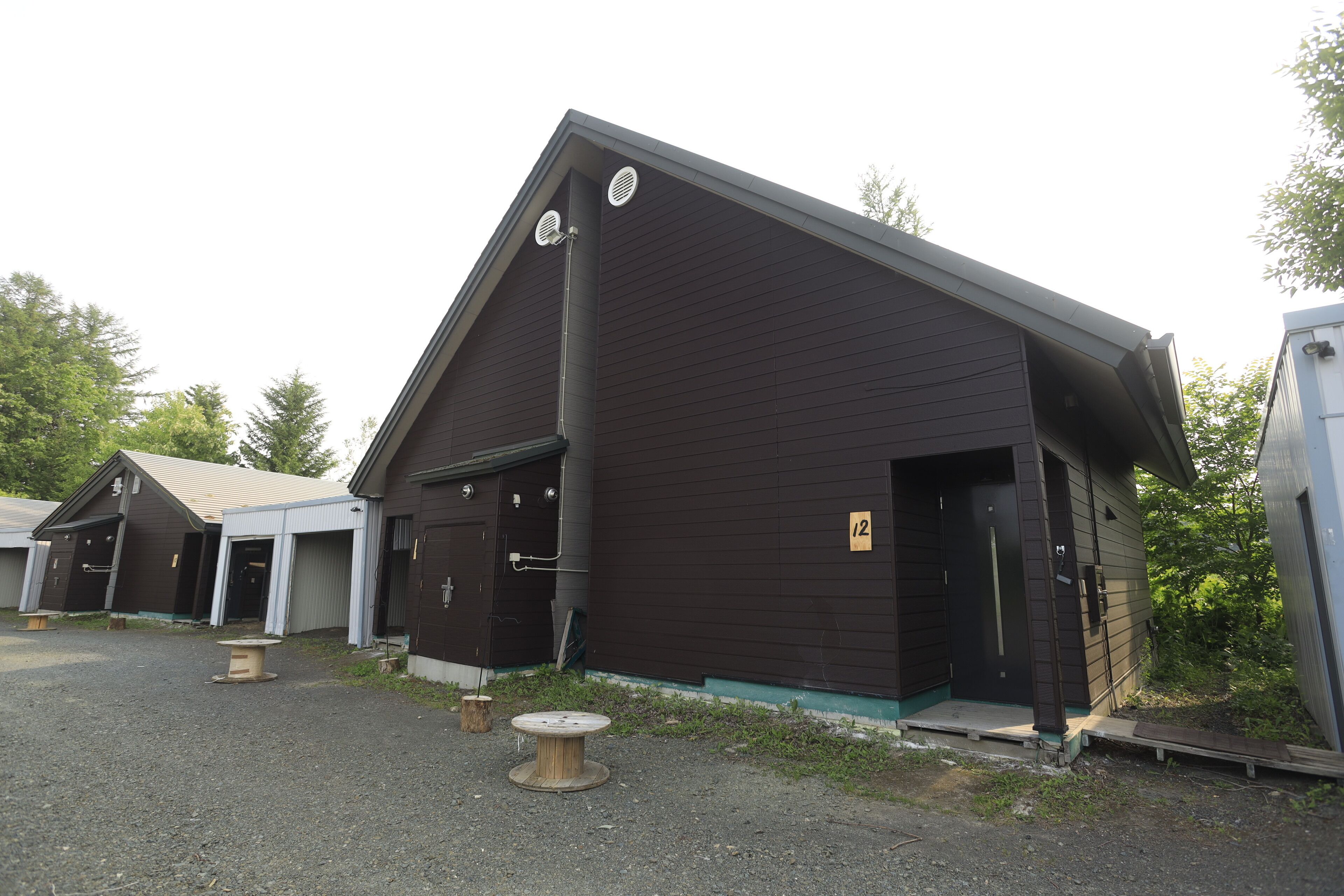 A building with a dark exterior, a door marked with the number 12, and a small outdoor seating area with a round table.
