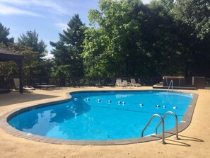 A swimming pool with a diving board, surrounded by lounge chairs and a covered seating area.