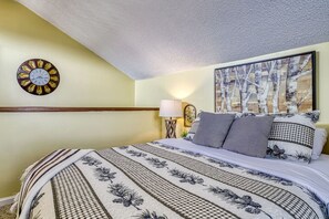 A bedroom with a large bed, a wall clock, a painting, and a lamp.