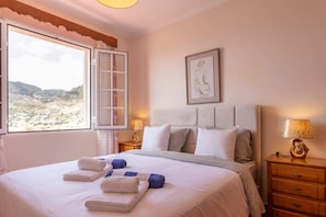 Una camera da letto con un letto, un comodino, una lampada, una finestra con vista e un quadro appeso al muro.