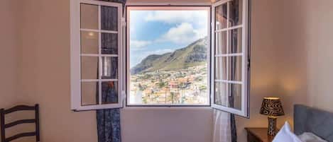 A hotel room with a bed, a chair, a nightstand with a lamp, and a window with open shutters.