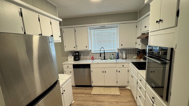 A modern kitchen with white cabinets, stainless steel appliances, and a wooden floor. - Gig ‘Em Getaway (Santa Anna)