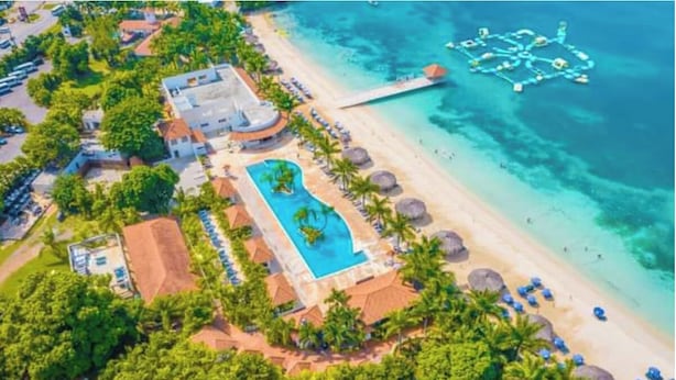 An aerial view of a resort with a swimming pool, beach, and a dock.