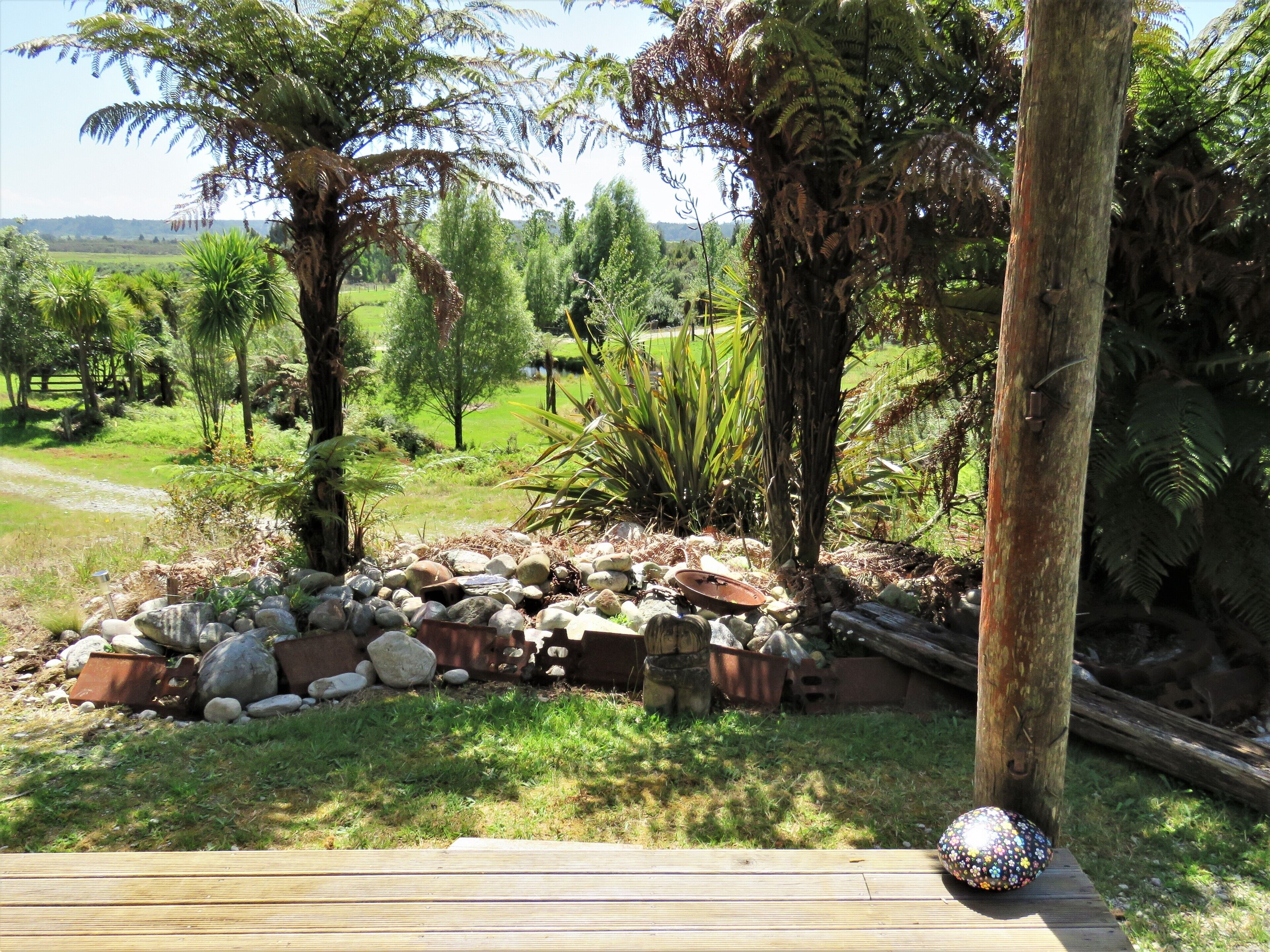 A garden with a wooden deck, rocks, and various plants.
