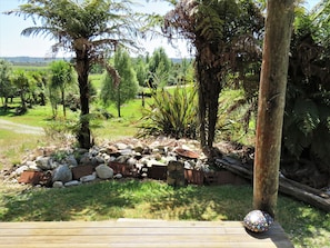 A garden with a wooden deck, rocks, and various plants. - GOLD NUGGET HUT - Off-grid Glamping Site on a farm in Hokitika (Arahura Valley)