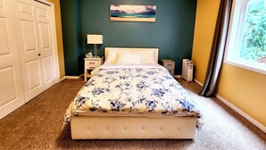 Un dormitorio con cama, mesitas de noche, una lámpara, un radiador y una ventana con cortinas.