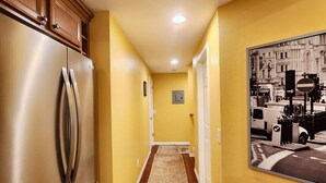 Un pasillo con un refrigerador de acero inoxidable, una alfombra estampada y un cuadro colgado en la pared.