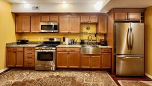 Una cocina con armarios de madera, electrodomésticos de acero inoxidable, encimera de granito y alfombra estampada.