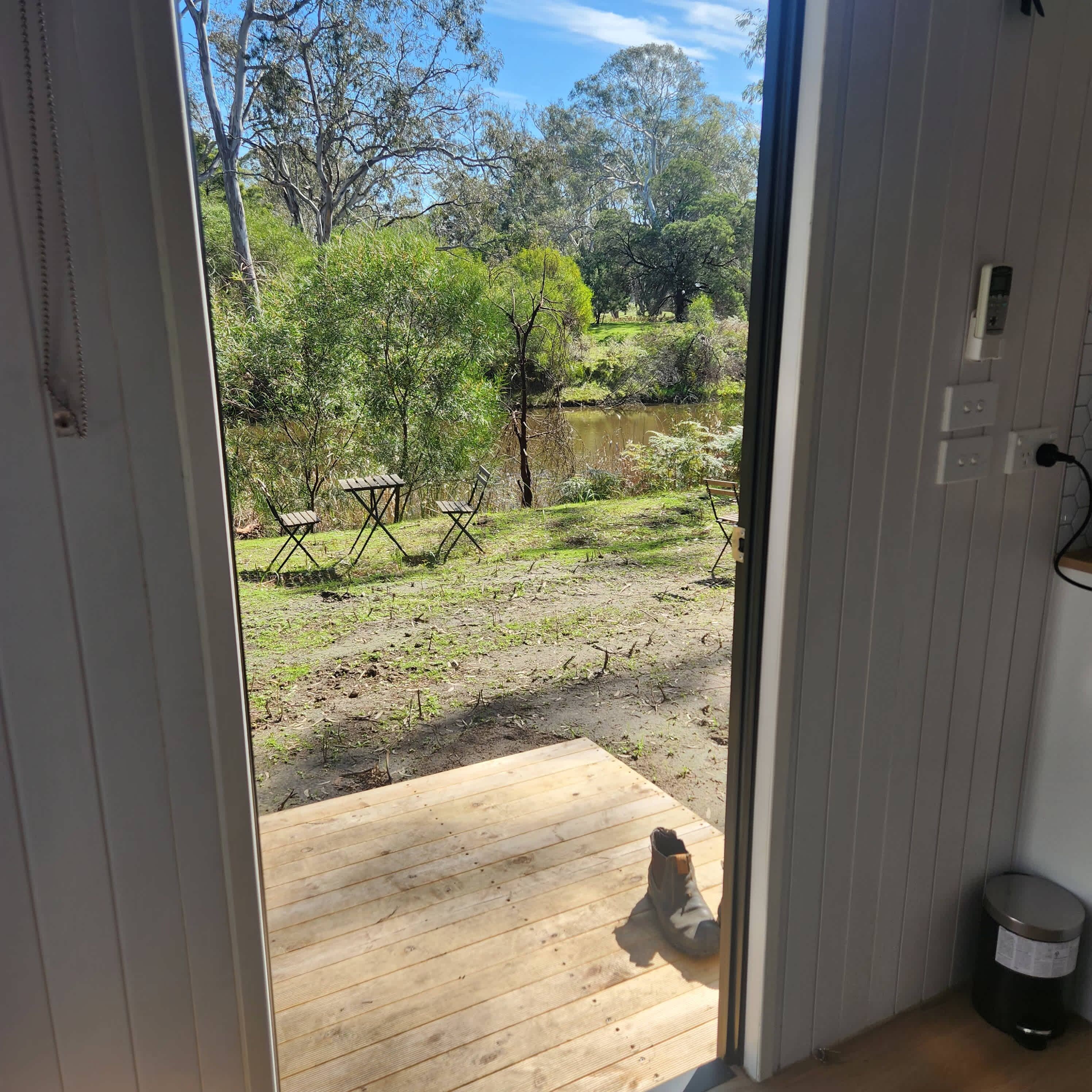 Vista desde una habitación con un balcón de madera que da a un área exterior con árboles y una masa de agua.