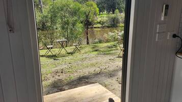 Vista desde una habitación con un balcón de madera que da a un área exterior con árboles y una masa de agua.
