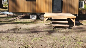 Una pequeña cabaña de madera con puerta corredera, una ventana y una mesa con bancos.