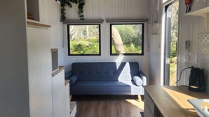 Un espacio habitable compacto con sofá, piso de madera y ventana con vista a zonas verdes.