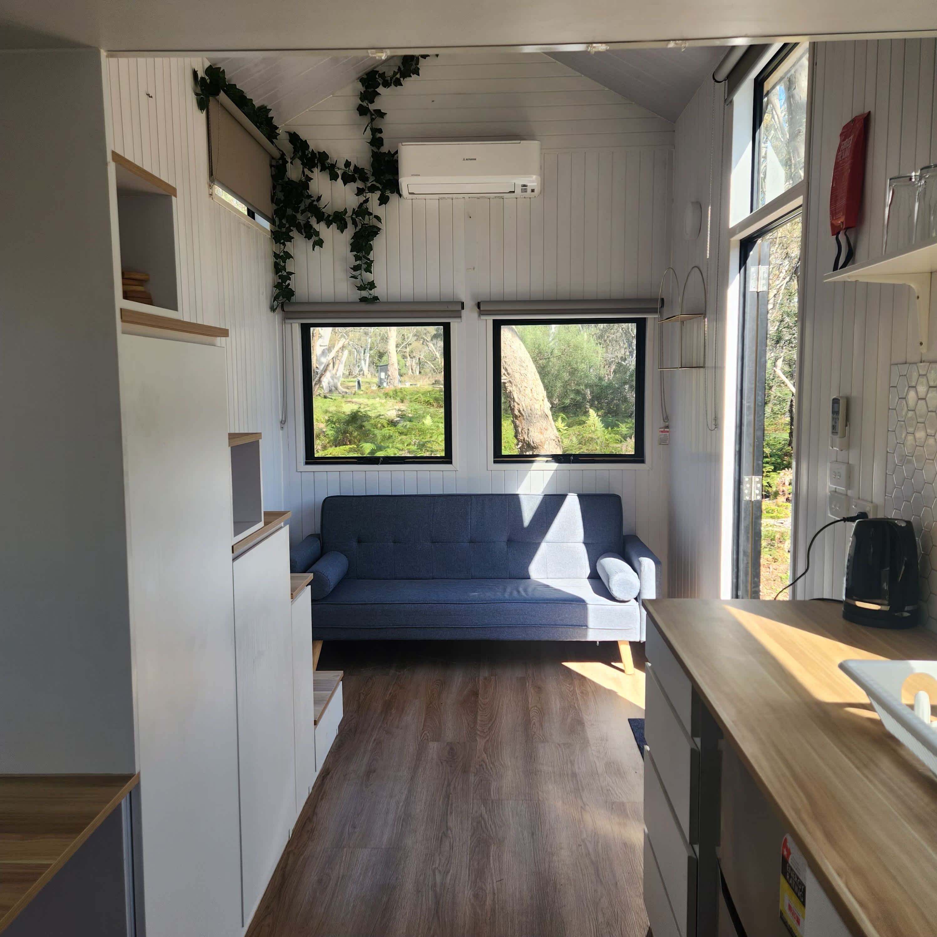 Un espacio habitable compacto con sofá, piso de madera y ventana con vista a zonas verdes.