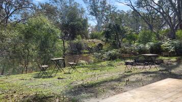 An outdoor area with a wooden table and chairs, surrounded by trees and a dirt path.