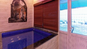 A spa area with a blue tiled pool, a tiger mural, and a window with a view of boats. - Auro Beach Resort (Vanur)