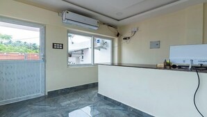A reception area with a marble floor, a reception desk, an air conditioning unit, and a window with a view of greenery outside. - Auro Beach Resort (Vanur)