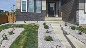 A two-story house with a stone foundation, a front porch, and a well-maintained lawn with gravel borders. - President's Choice: Executive Guest Lodge | AC | Yard (Edmonton)