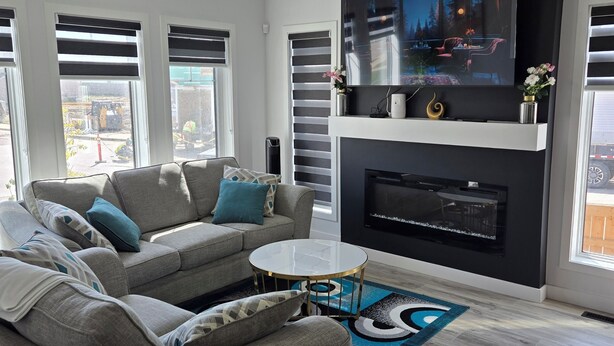 A modern living room with a grey sofa, a glass coffee table, and a flat-screen TV mounted on a black wall. - President's Choice: Executive Guest Lodge | AC | Yard (Edmonton)