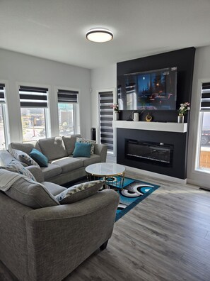 A modern living room with a grey sofa, a glass coffee table, and a flat-screen TV mounted on a black wall. - President's Choice: Executive Guest Lodge | AC | Yard (Edmonton)