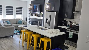 A modern kitchen with a central island, bar stools, and a dining area with a sofa. - President's Choice: Executive Guest Lodge | AC | Yard (Edmonton)