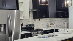 A modern kitchen with dark cabinets, stainless steel appliances, a central island with stools, and pendant lighting. - President's Choice: Executive Guest Lodge | AC | Yard (Edmonton)