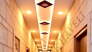 A hotel corridor with a polished floor, potted plants, and a central light fixture. - Hotel Pleasure Haveli (Jaisalmer)