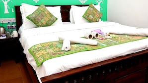 A neatly made bed with a green patterned bedspread, two decorative pillows, and a rolled towel on the bed. - Hotel Pleasure Haveli (Jaisalmer)