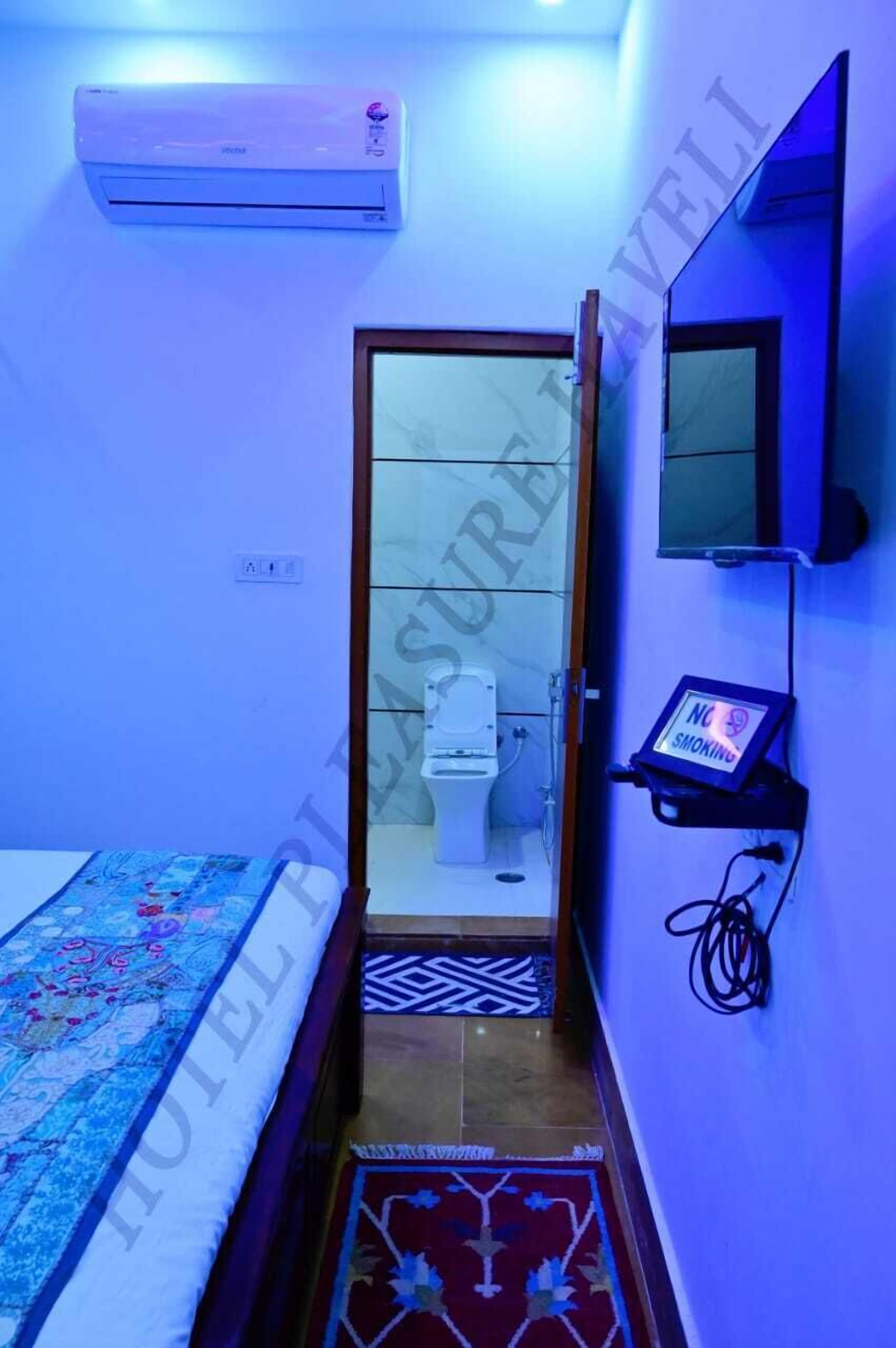 Een kleine hotelkamer met een bed, een wandairconditioner, een klein plankje met een ‘Niet roken’-bord, en een badkamer die door een geopende deur zichtbaar is.