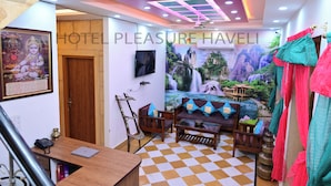 A hotel room with a checkered floor, a sofa set, a TV, a mural of a waterfall, and a ceiling with recessed lighting. - Hotel Pleasure Haveli (Jaisalmer)