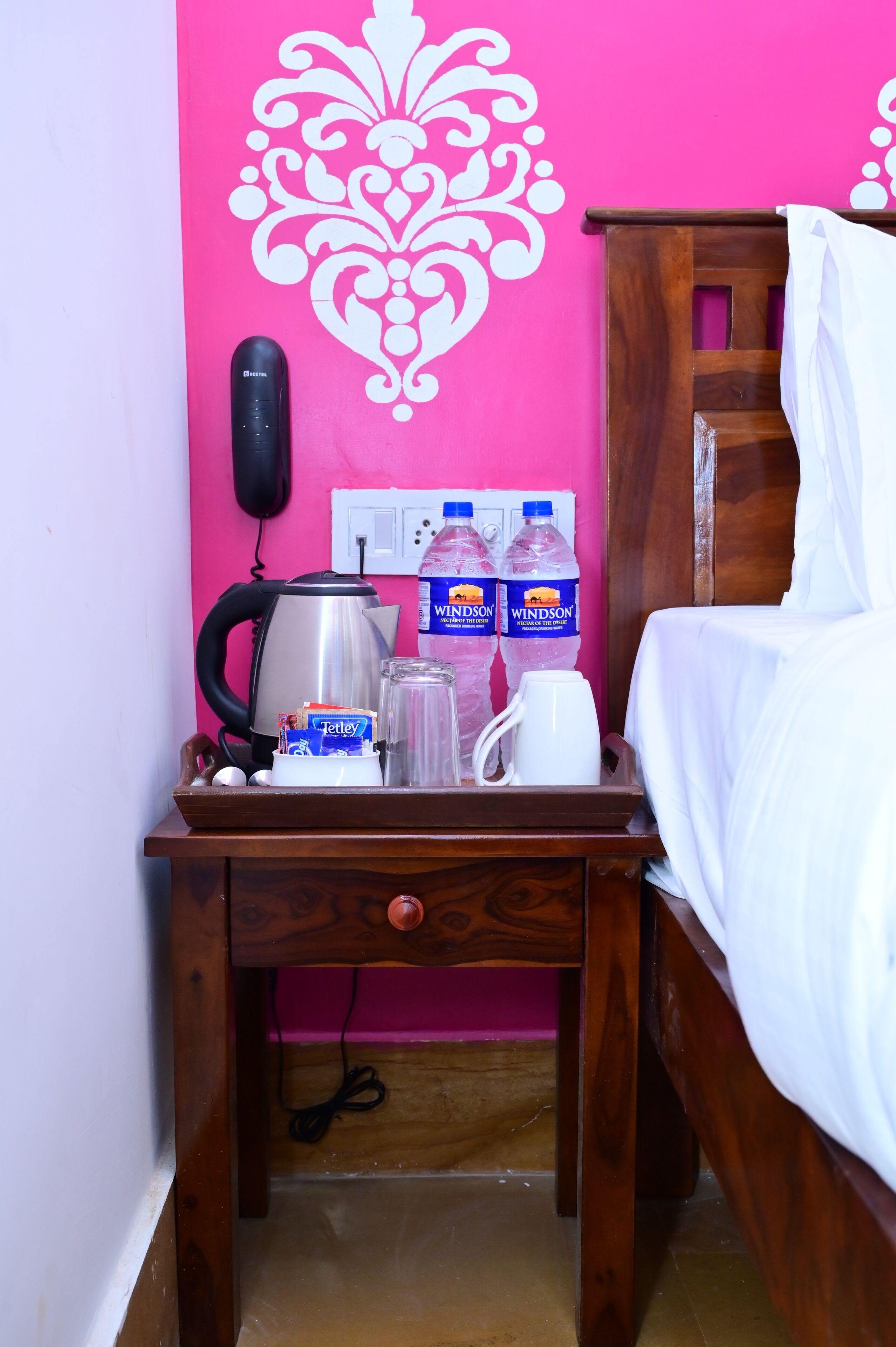 A wooden nightstand with a kettle, two bottles of water, a jug, and a box of tissues.
