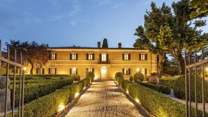 A two-story building with a symmetrical facade, a central entrance, and a gravel pathway flanked by neatly trimmed hedges. - Elegant historic residence in the hills of Val d'Orcia (Montepulciano)