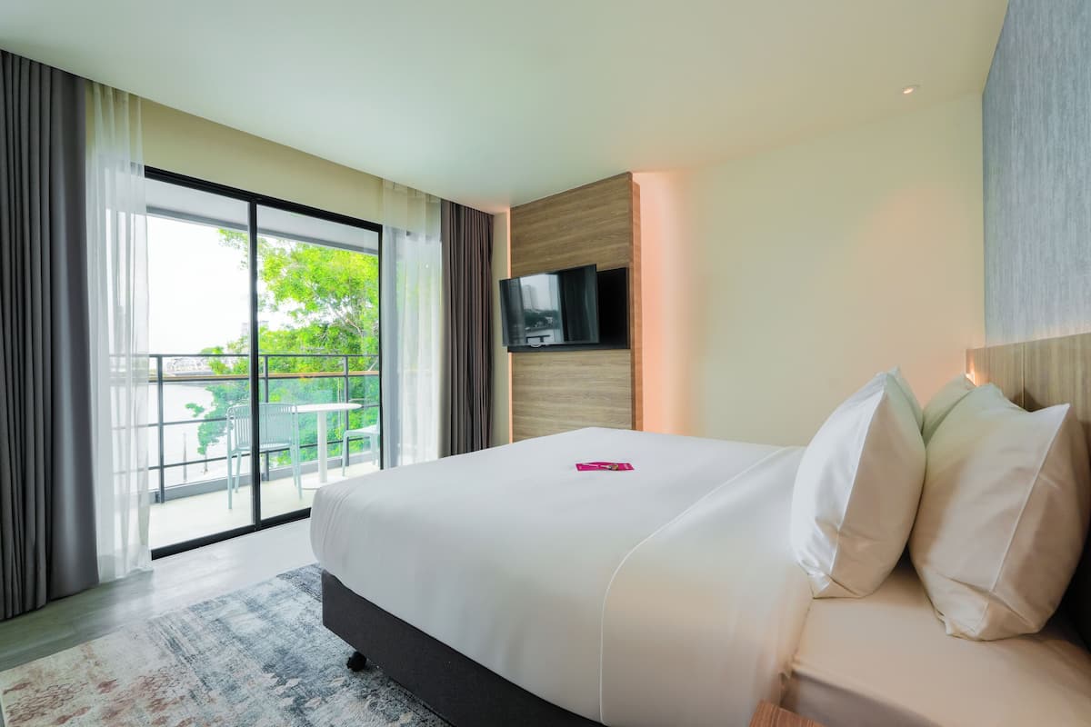 A modern hotel room with a large bed, a flat-screen TV mounted on the wall, and a balcony with outdoor seating.